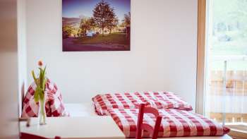 Cozy double room in the guest house at Camping Mittagsspitze with red and white checkered bed linen and decoration.