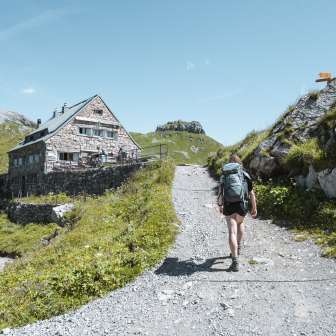 Woman with backpack on a mountain path shortly before the Pfälzer hut - alpine scenery, marked hiking route and green high mountain meadows