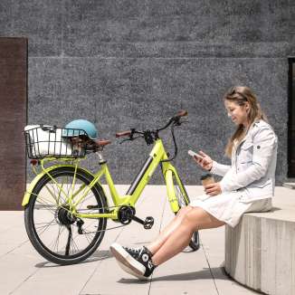 Young woman sits with coffee and smartphone next to a yellow e-bike in the urban center of Vaduz