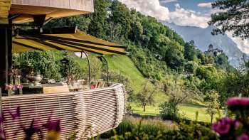 Sunny terrace with blooming flowers and elegantly laid tables with a view of the valley