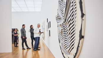 A group of visitors in the art museum's exhibition hall; in the foreground is a large, round work of art