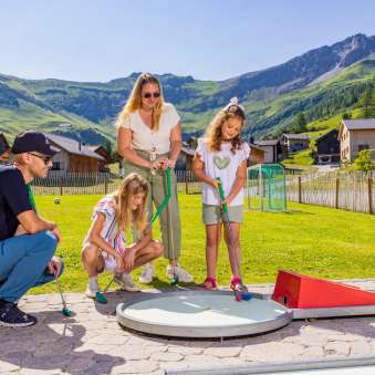 Family playing minigolf together in the sunny mountain village of Malbun in Liechtenstein - fun for young and old in the Alps.