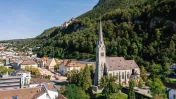 Aerial view of St. Florin's Cathedral in Vaduz with Vaduz Castle in the background on a sunny day.