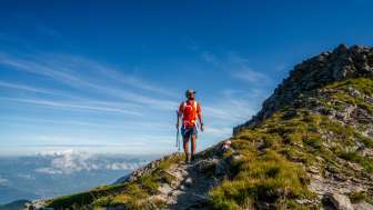 Hiker with a red shirt on the ridge of the Drei Schwestern mountain chain along Route 66 with a view over the Alpine landscape in Liechtenstein