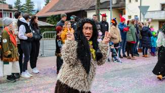 Disguised Schaan witch at the carnival parade in Schaan, Liechtenstein, in front of an audience and colorful confetti on the street