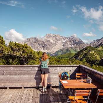 Hiker gazing at an impressive Alpine panorama from the wooden terrace by the viewing platform.