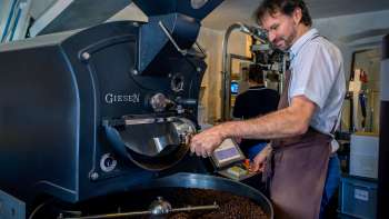 Man roasting coffee beans on a modern roasting machine in a coffee roasting plant