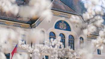 Facade of the government building in Vaduz, framed by white blossoming trees in spring.