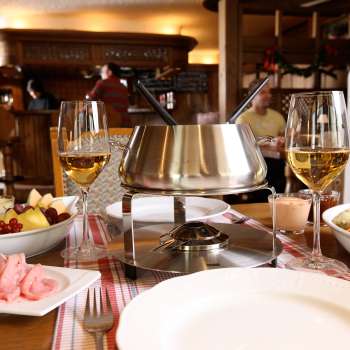 Close-up of cheese fondue set with fresh bread, vegetables and wine in a stylish setting