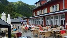 Sunny terrace of the restaurant with covered tables, parasols and views of the Alps.