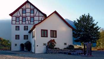 Historic building ensemble of the Pfrundbauten with half-timbered façade and mountain backdrop in Liechtenstein in the evening light.