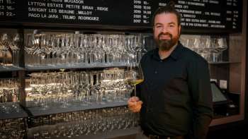Friendly bartender of the WY Weinbar with wine glass in front of a stylish shelf full of glasses and wines.