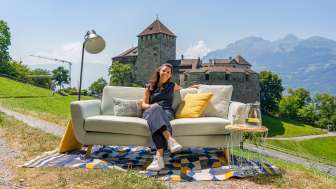 Woman sitting on a sofa with a view of Vaduz Castle and the mountains of Liechtenstein, modern outdoor ambience with decoration