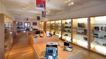 View into a bright exhibition room of the Lawena Museum with illuminated display cases full of historical electrical appliances.