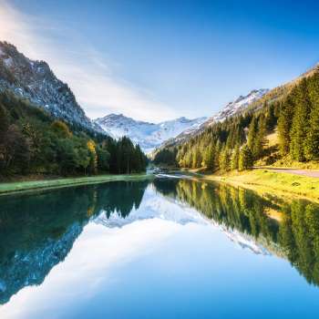 Gänglesee lake in Steg with mountain reflection, surrounded by forest, sunbeams over the slope.