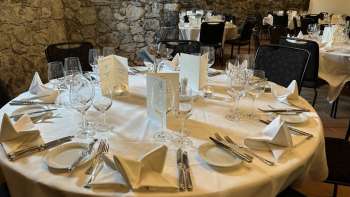 Elegantly laid round table with white tablecloths, napkins and menus in front of a stone wall.