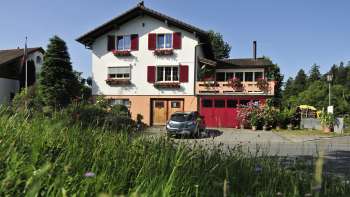 Charming exterior view of Bed & Breakfast Büchel with red shutters and flower meadow in the foreground.