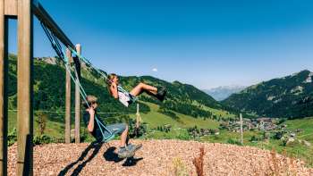 Two children swinging with a view of Malbun