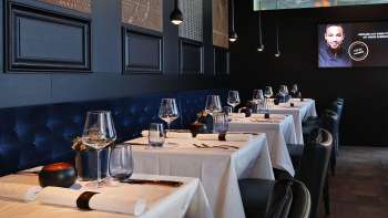 Elegant interior of the Esquire Bar & Bistro in Vaduz with stylishly laid tables, dark blue upholstered bench and atmospheric lighting.