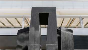 Sculpture "Progression of a Form in 3 Stelae" by Christian Megert made of black stone in front of a modern glass façade in Vaduz.