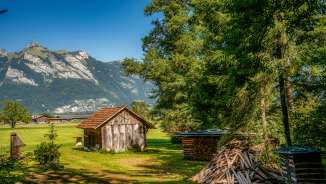 Small wooden barn on a meadow with a pile of firewood and a view of the Alps along Route 66 in Liechtenstein