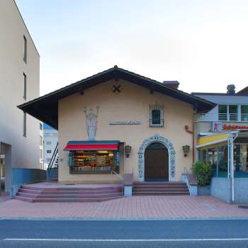 Exterior view of the Altes Kino Vaduz with lettering above the entrance and red awnings, located between two modern buildings.