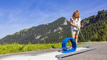 Girl concentrates on a blue looping course in an alpine setting while playing mini golf