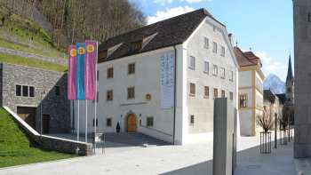 Exterior view of the Liechtenstein NationalMuseum in Vaduz with colorful flags and a view of the historic façade.