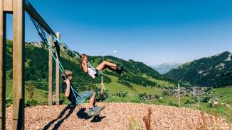 Two children swinging on a mountain playground with a view over the summer panorama of Malbun in Liechtenstein