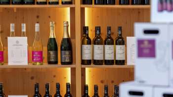 Interior of the Court Winery with stylishly illuminated wooden shelves full of wine bottles and cartons.
