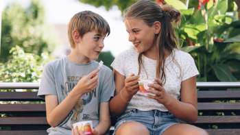 Two children enjoying an ice cream on a wooden bench in front of the ice cream shop