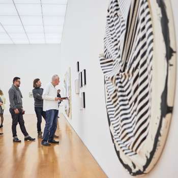 Group of visitors in the exhibition room of the Art Museum, in the foreground a large, round work of art