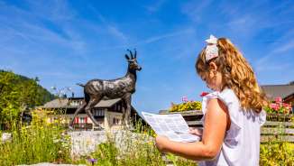 Girl with map in front of the chamois statue in Malbun - child-friendly exploration tour in the family vacation resort in Liechtenstein.