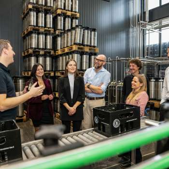 Group of visitors on a guided tour of the brewery's barrel warehouse with explanations from a brewery employee.