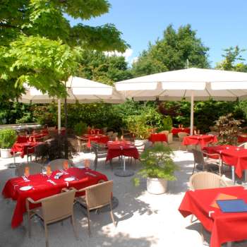 Exterior view of the terrace with red tablecloths, surrounded by trees and parasols.