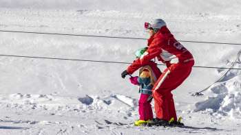 A ski instructor rides the platter lift with a child