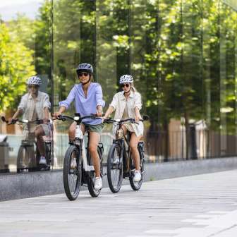 Two women on e-bikes ride through the modern center of Vaduz in Liechtenstein, with its glass façade and urban flair