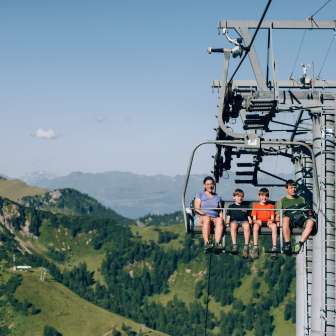 Family with children on a chairlift above the green mountains of Malbun - summer adventure and panoramic views in Liechtenstein