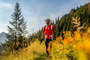 Hiker with a red shirt on a sunny mountain path near Malbun, surrounded by meadow flowers, coniferous forest and alpine scenery in Liechtenstein