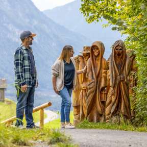 Couple looking at carved wooden figures on the Walser Legend Trail in Triesenberg with a view of the valley and mountains in the background