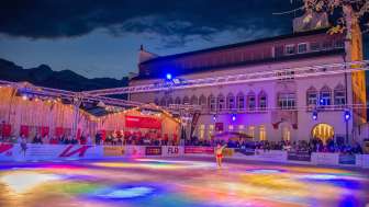 Colorful ice rink at "Vaduz on Ice" with light show and skater in front of the government building in Liechtenstein