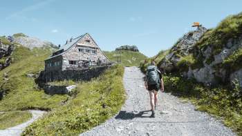Hiker with rucksack walking along a mountain path towards the Pfälzer hut in the Liechtenstein Alps.