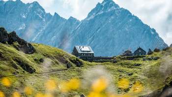 View of the Pfälzer hut, situated on a green alpine pasture in front of steep rock faces in the Liechtenstein Alps.