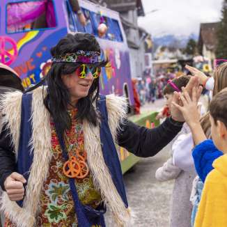 Hippie dressed up at the children's carnival in Mauren, high-fives with children in front of a colorful float.