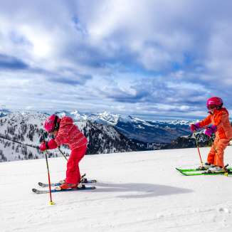 Two children skiing in Sareis, with a view of snow-covered mountains and wintry landscape.