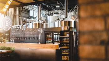 Interior view of a brewery with stainless steel brewing system and inviting bar in the foreground.