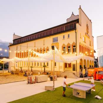 Vaduz Town Hall Square in the evening during a busy market day with crowds of people, stalls and atmospheric lighting.