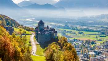 Vaduz Castle with a view of the Rhine Valley and mountain landscape.