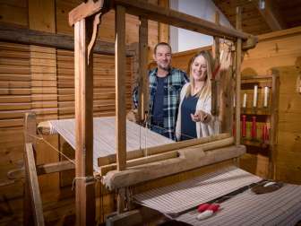 A couple looks at a functioning historical loom in the Walser Museum Triesenberg in Liechtenstein, surrounded by wood paneling