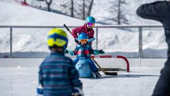 Family ice skating in Malbun, child sitting on an animal-shaped skating aid.